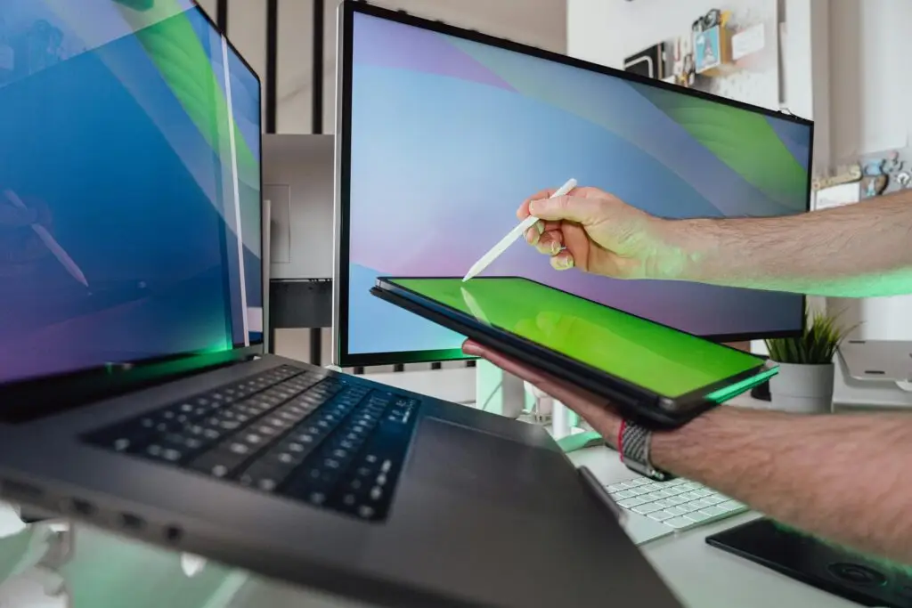 A person using a stylus on a tablet in a tech-savvy workspace with dual monitors